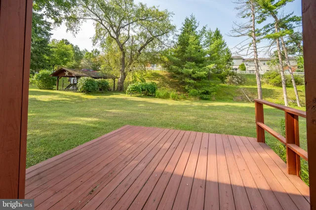 a view of a yard with wooden deck and large trees