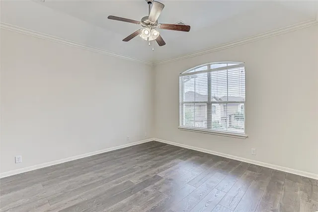 an empty room with wooden floor ceiling fan and windows