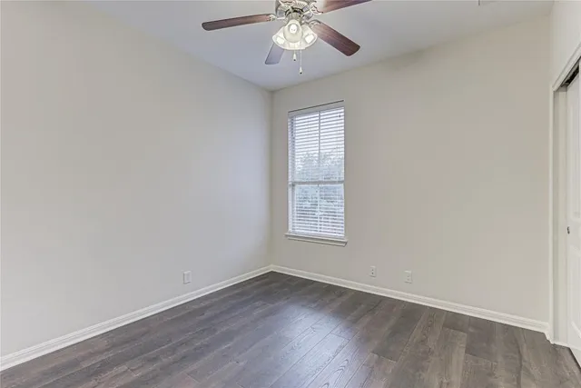 an empty room with wooden floor chandelier fan and windows