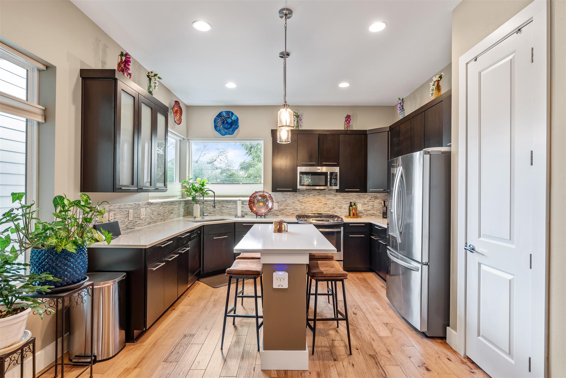 The chef-inspired kitchen is bathed in natural light from corner windows and features sleek quartz countertops, stainless-steel appliances, abundant cabinetry, a spacious pantry, and a center island with bar seating.