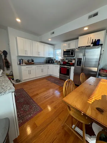 a kitchen with stainless steel appliances granite countertop a sink a stove white cabinets a dining table and chairs