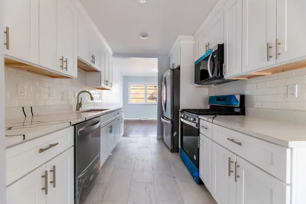 a kitchen with stainless steel appliances granite countertop white cabinets a sink a stove a microwave and wooden floors