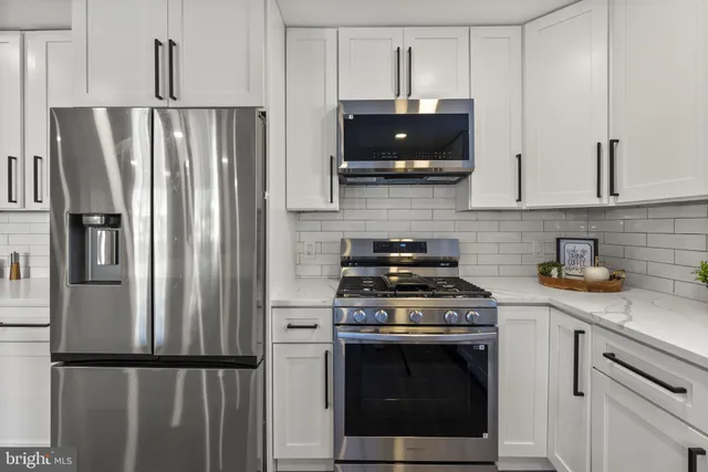 a large kitchen with kitchen island a stove a sink a refrigerator and white cabinets with wooden floor