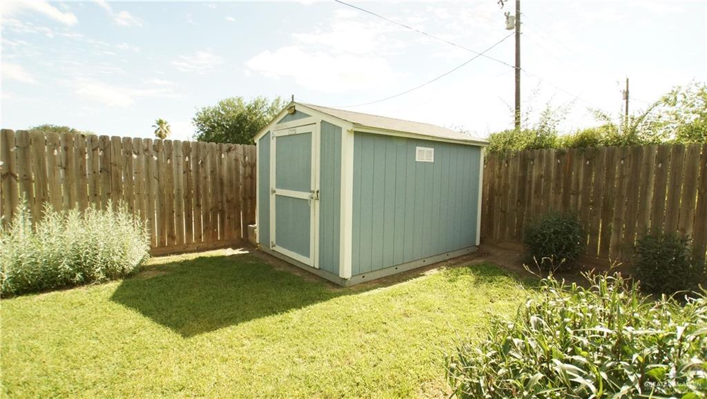 414 Ric Mar Street Edinburg, TX 78541 - Photo 7 of 36 Backyard featuring a light blue storage shed, a wooden privacy fence, and green lawn