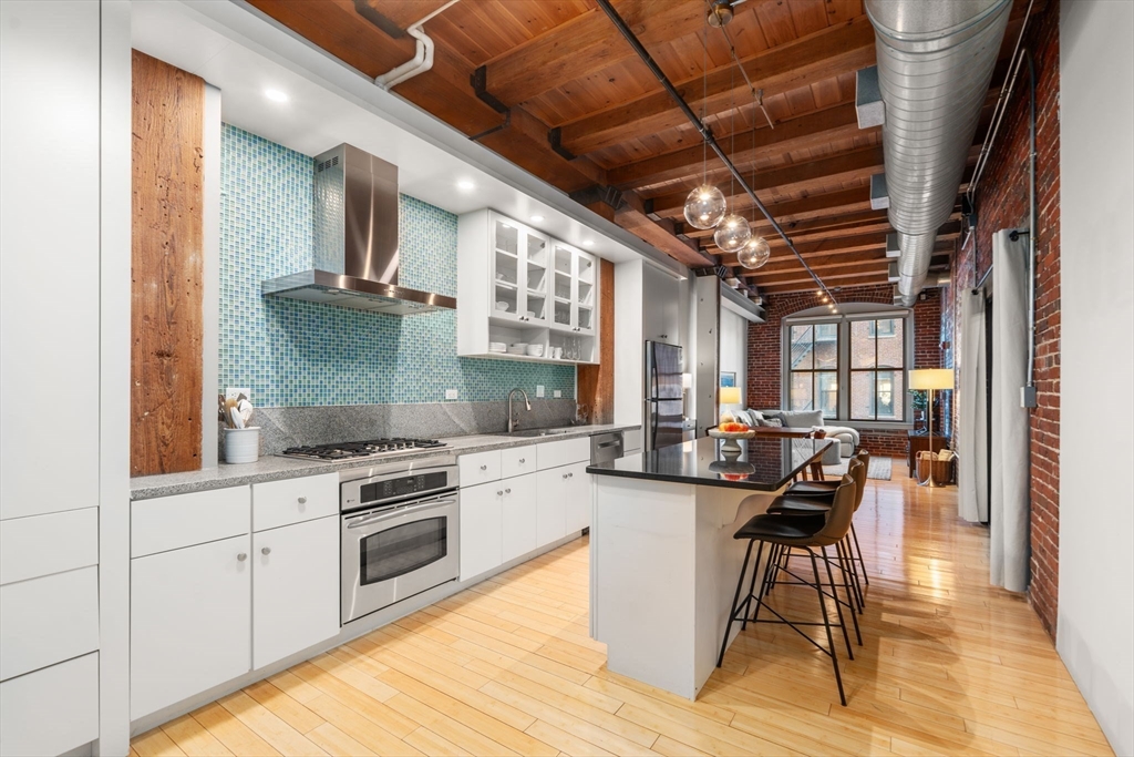 a kitchen with stainless steel appliances granite countertop a stove top oven a sink dishwasher and white cabinets with wooden floor