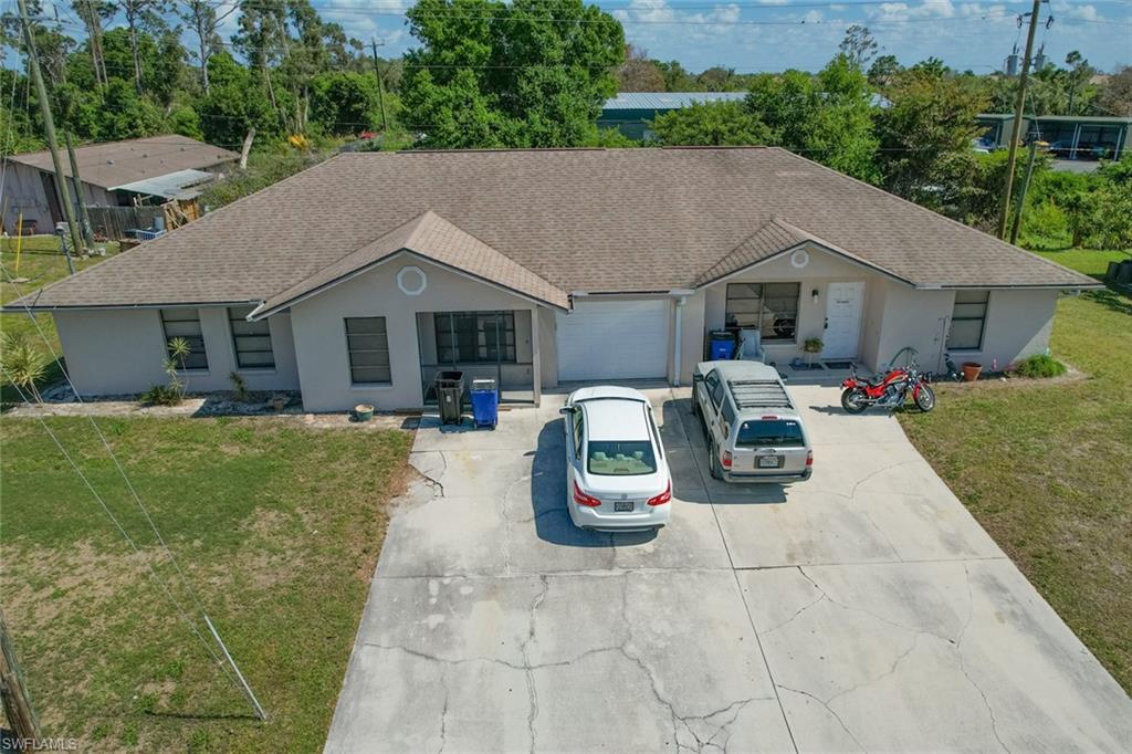 Ranch-style home featuring a front lawn, stucco siding, a shingled roof, and driveway
