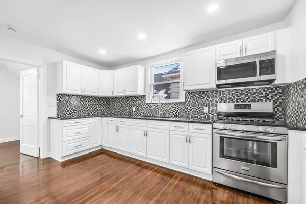 a kitchen with granite countertop wooden floor stainless steel appliances and white cabinets