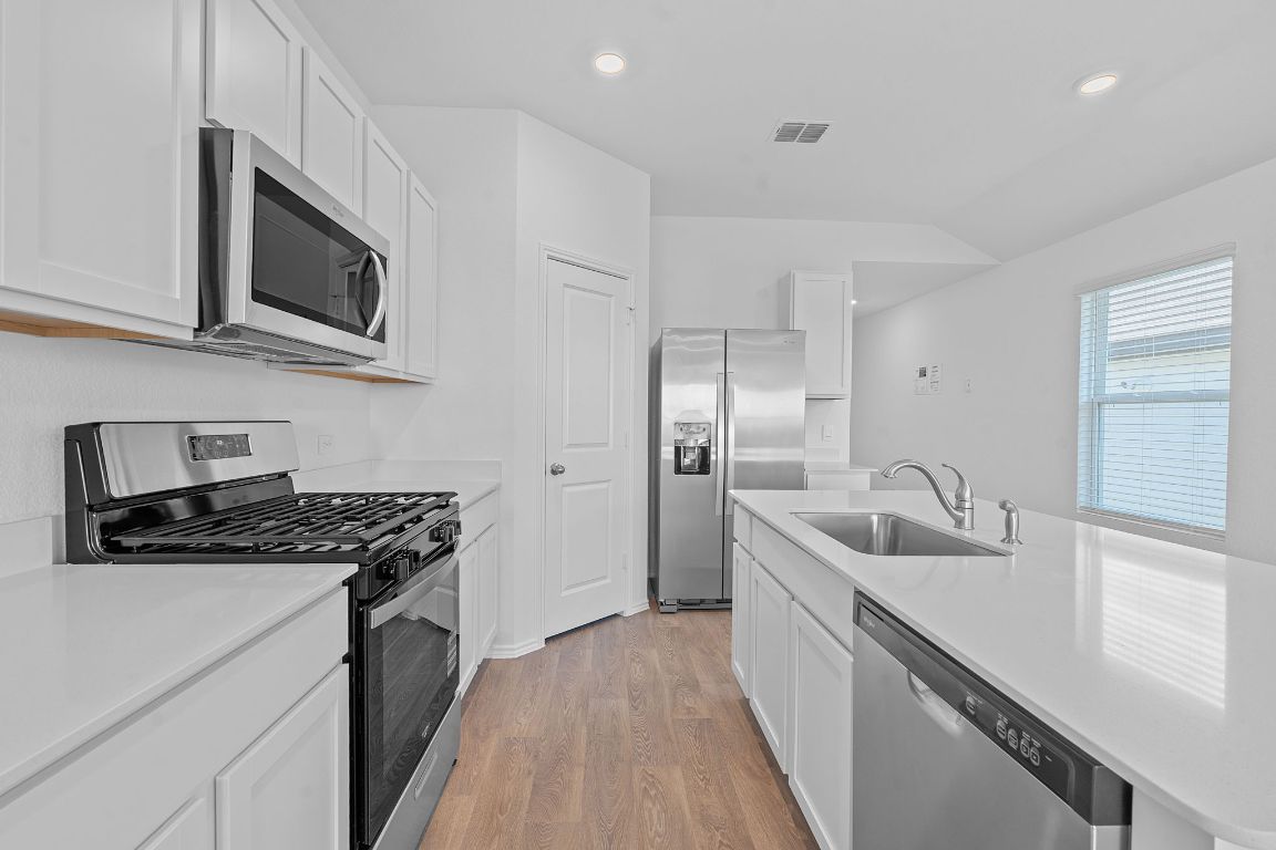 13309 Mancos Shale Road Mustang Ridge, TX 78610 - Photo 6 of 19 Kitchen featuring appliances with stainless steel finishes, recessed lighting, light wood finished floors, white cabinets, and light stone counters