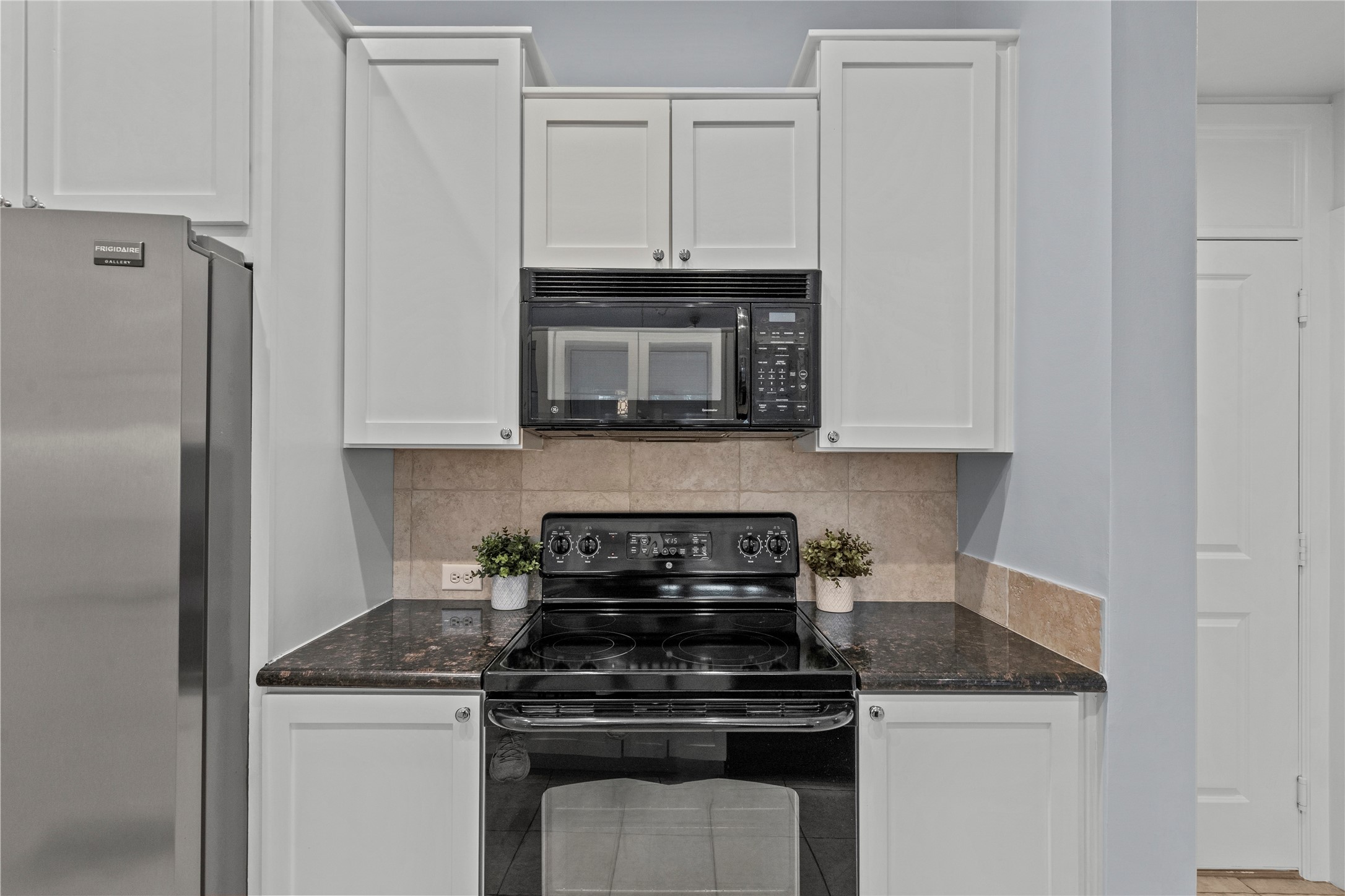 1900 Genesee Street, Unit 203 Houston, TX 77006 - Photo 14 of 30 This kitchen features sleek black and stainless steel refrigerator, white cabinetry, and dark countertops. The space is accented with neutral-toned backsplash tiles, offering a modern and clean look.