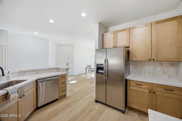 a kitchen with stainless steel appliances granite countertop a refrigerator a sink a stove and white cabinets with wooden floor