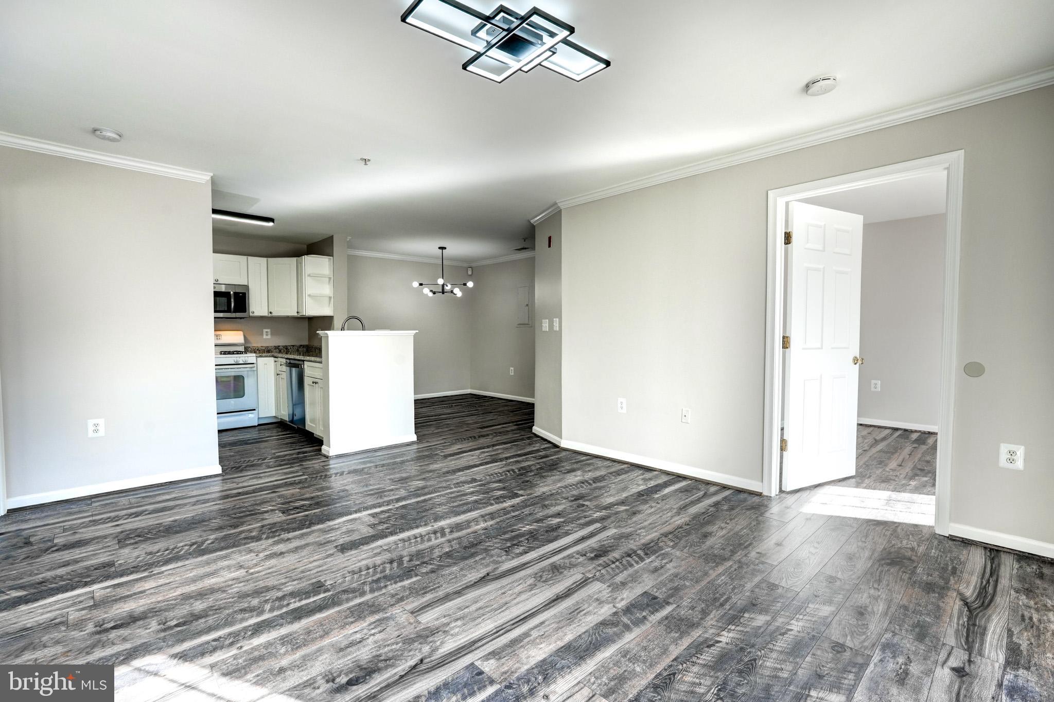 a view of empty room with wooden floor and kitchen view