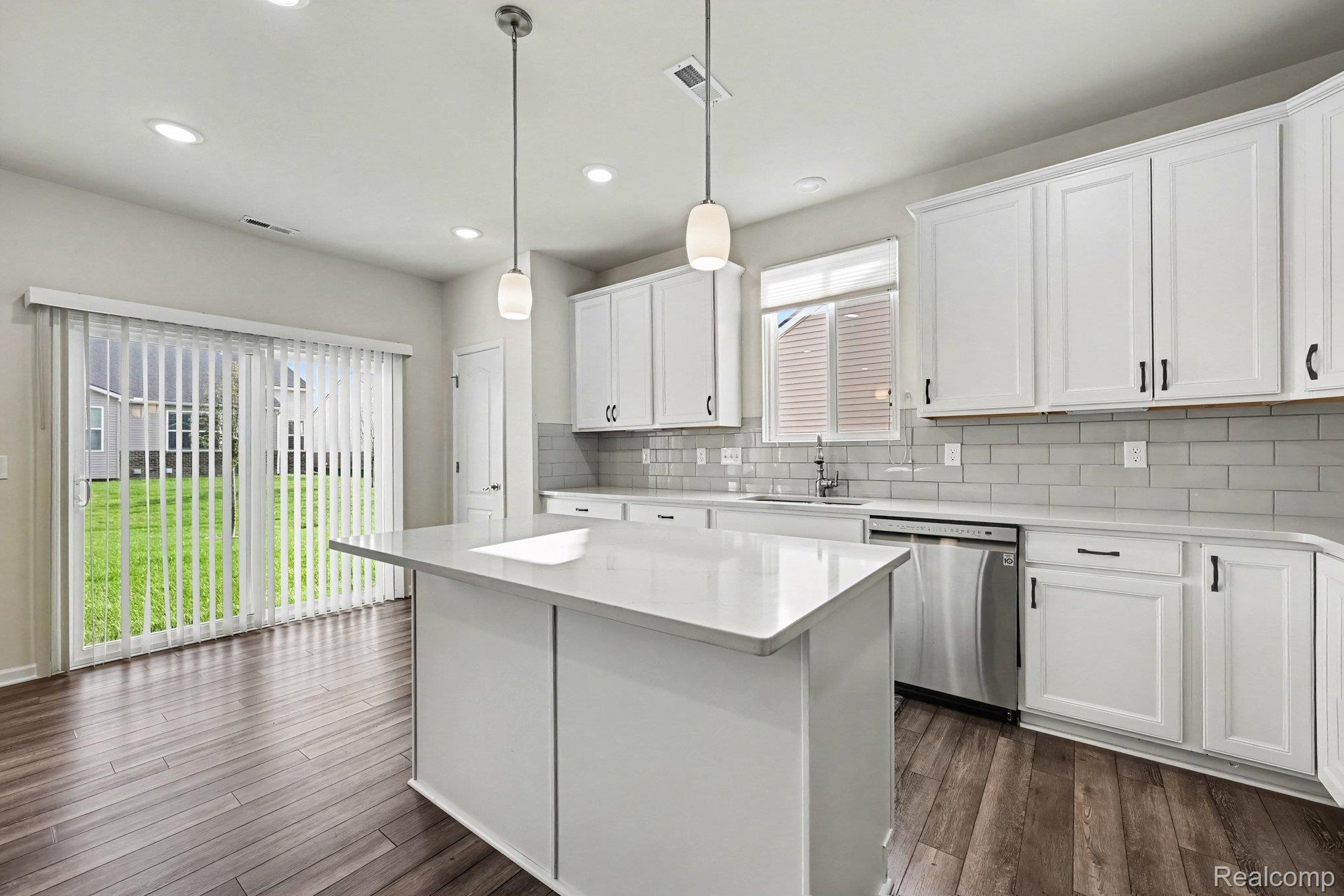 50153 Fowler Road Canton, MI 48188 - Photo 11 of 27 Kitchen featuring a center island with a light-colored countertop, white cabinetry with dark hardware, stainless steel dishwasher, subway tile backsplash, and wood-finish flooring