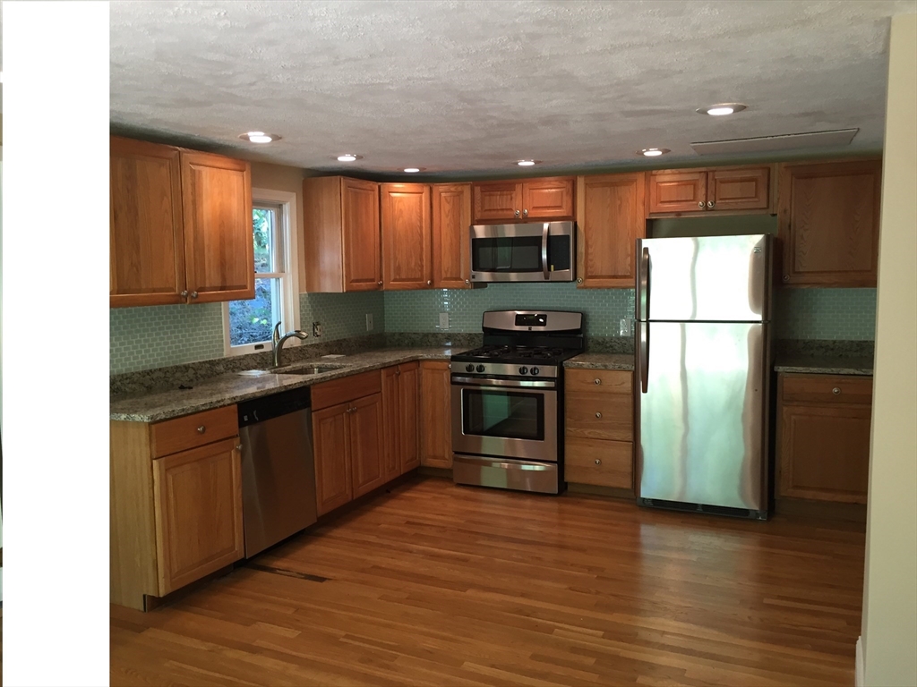 a kitchen with stainless steel appliances granite countertop a refrigerator a sink a stove a microwave and wooden floor