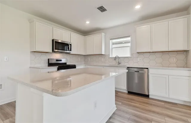 a kitchen with stainless steel appliances granite countertop a sink a stove a microwave and white cabinets