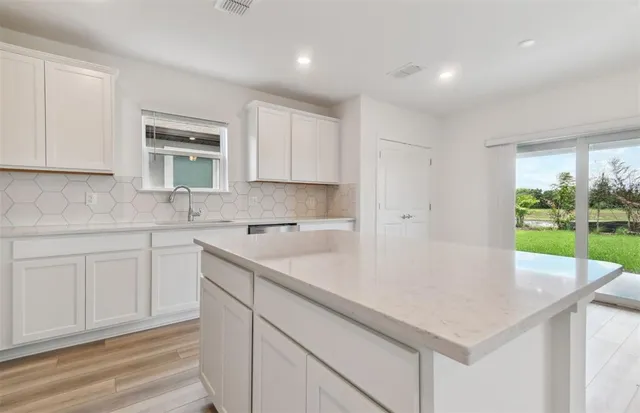 a kitchen with a sink dishwasher and white cabinets with wooden floor