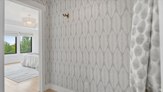 2038 East Ranch Road Eagle Mountain, UT 84005 - Photo 20 of 66 Light wood-finish flooring extends from the hallway into the room, featuring a tiered crystal chandelier, expansive windows, and a decorative botanical wallpaper accent wall