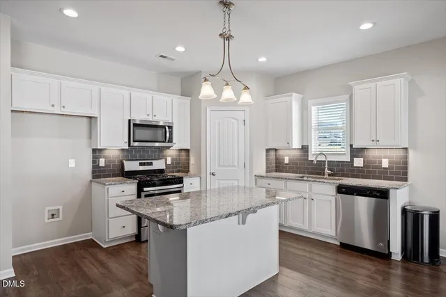 a kitchen with stainless steel appliances granite countertop a sink stove a refrigerator a center island with wooden floor and cabinets