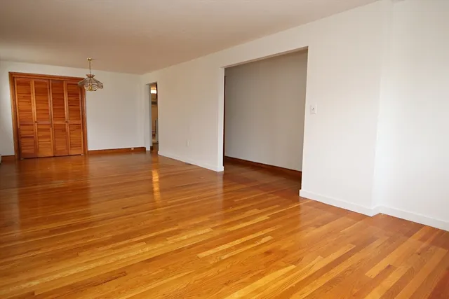 a view of an empty room with wooden floor and a refrigerator