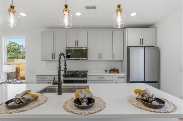 a kitchen with stainless steel appliances kitchen island a refrigerator a stove a dining table and chairs with wooden floor