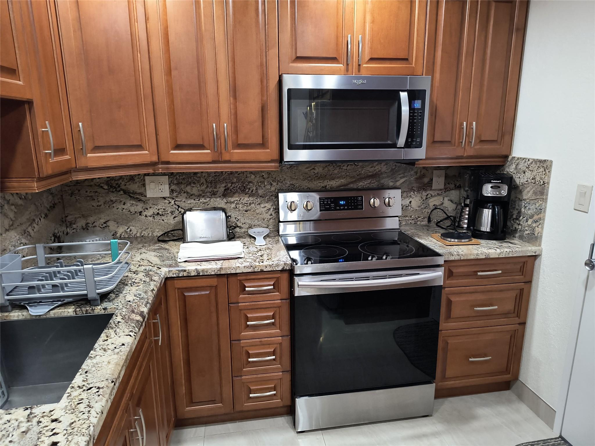 10777 West Sample Road, Unit 402 Coral Springs, FL 33065 - Photo 18 of 27 a kitchen with granite countertop wood cabinets and stainless steel appliances