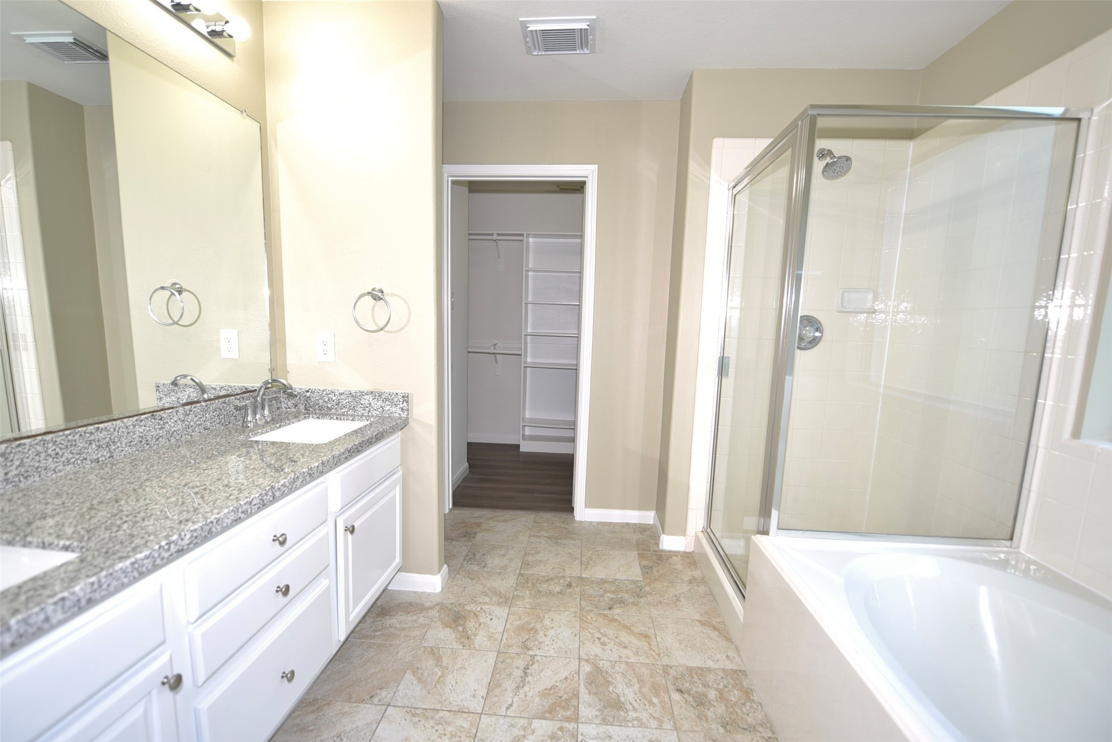 9611 Babbling Spring Court Tomball, TX 77375 - Photo 16 of 31 This bathroom features a dual-sink granite vanity, a glass-enclosed shower, and a separate bathtub. It includes a spacious walk-in closet and tile flooring, offering a modern and functional space.