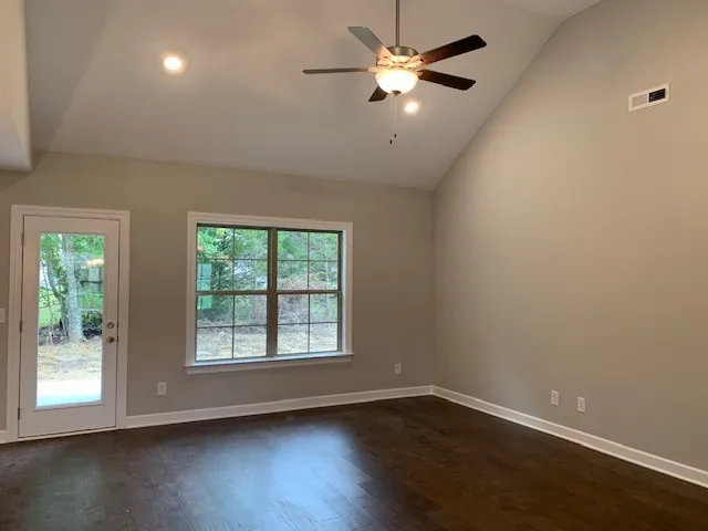 an empty room with wooden floor fan and windows