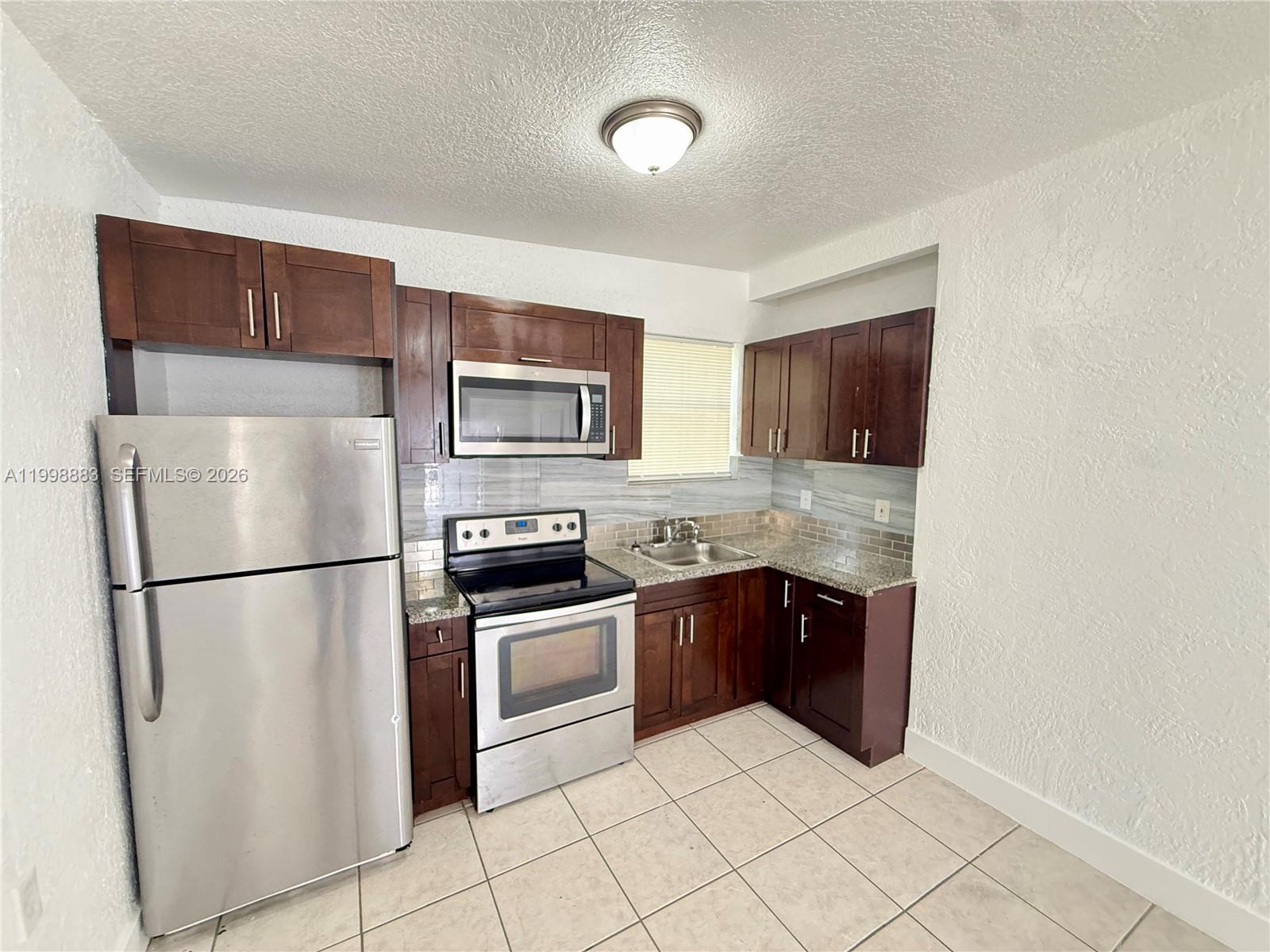 1345 Northwest 55th Street, Unit 2 Miami, FL 33142 - Photo 3 of 9 a kitchen with granite countertop a refrigerator and a stove top oven