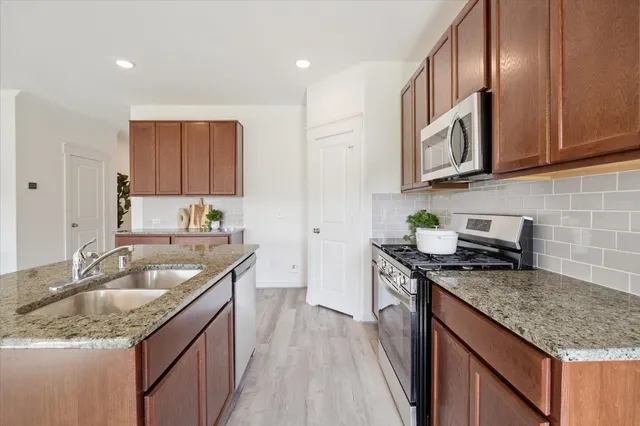 a kitchen with granite countertop stainless steel appliances a sink stove and cabinets