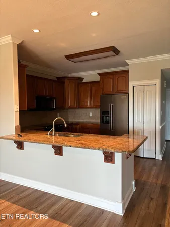 a kitchen with stainless steel appliances granite countertop a refrigerator and a sink with wooden floors