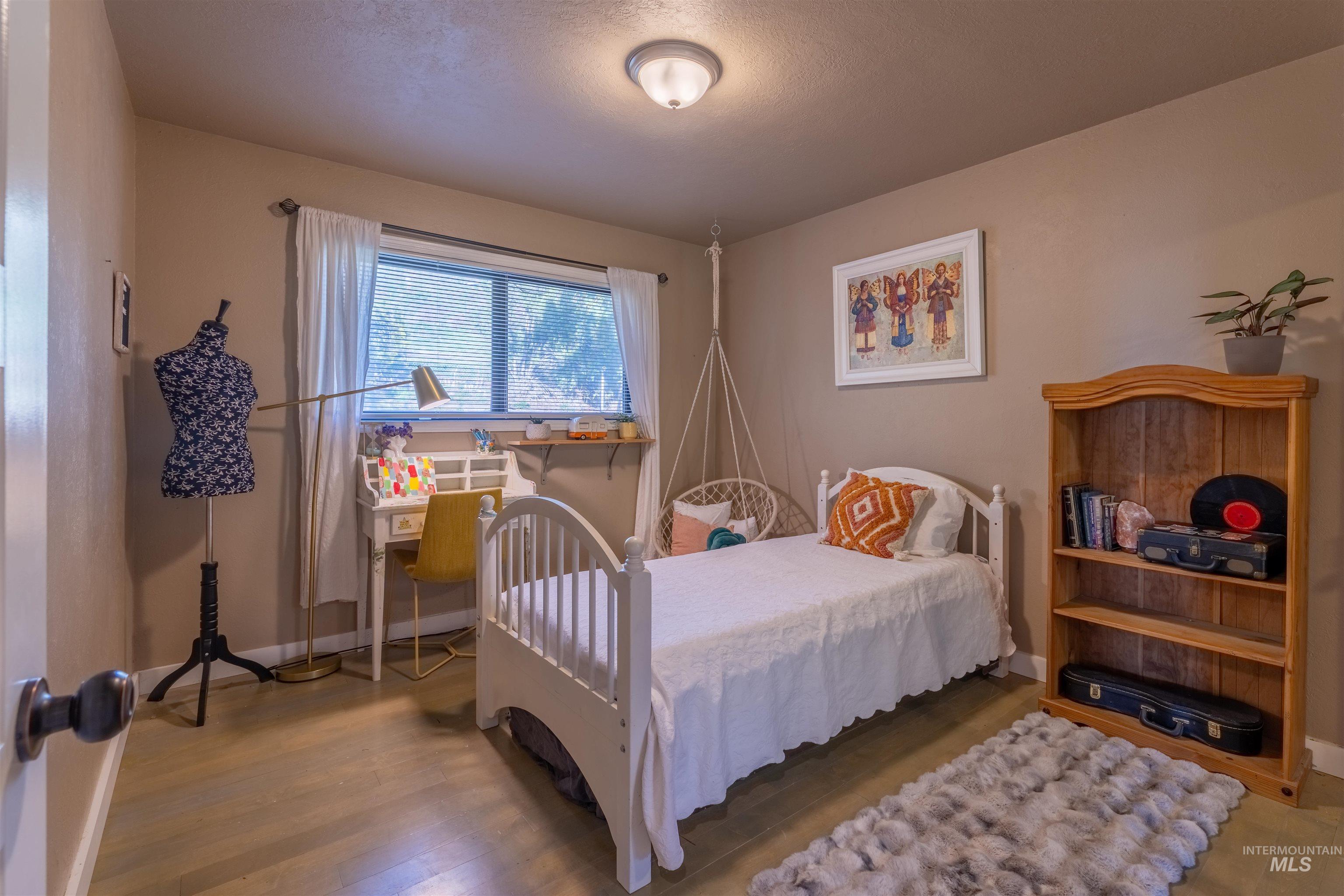 14526 Perfection Lane Caldwell, ID 83607 - Photo 13 of 24 Bedroom featuring light wood-finish flooring, a window with exterior tree-lined scenery, and a built-in overhead light fixture