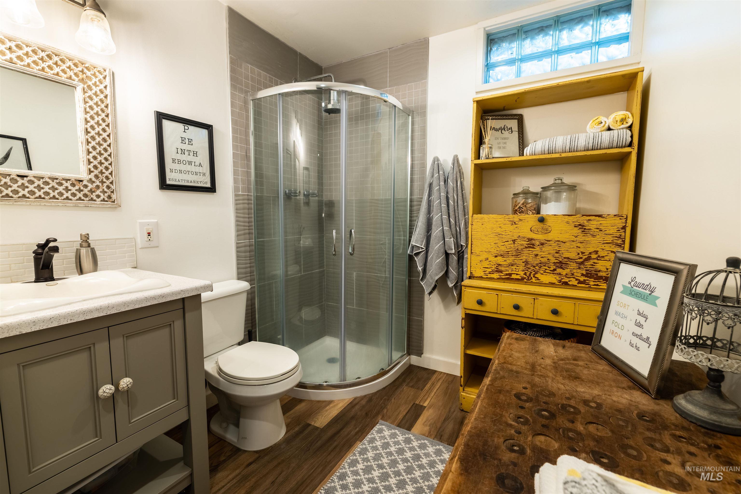 14526 Perfection Lane Caldwell, ID 83607 - Photo 15 of 24 Bathroom featuring a corner glass-enclosed shower, wood-finish flooring, a vanity with cabinet storage, a white basin sink, and a glass block window