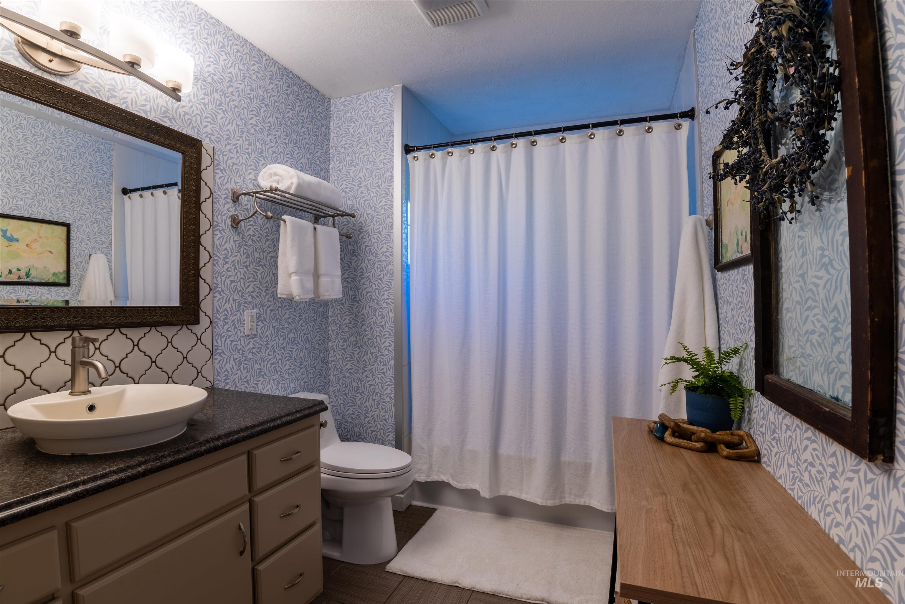 14526 Perfection Lane Caldwell, ID 83607 - Photo 10 of 24 Bathroom featuring a shower with a white curtain, a vanity with a vessel sink and dark countertop, a decorative mirror with an ornate frame, mosaic tile backsplash, and wood-finish flooring