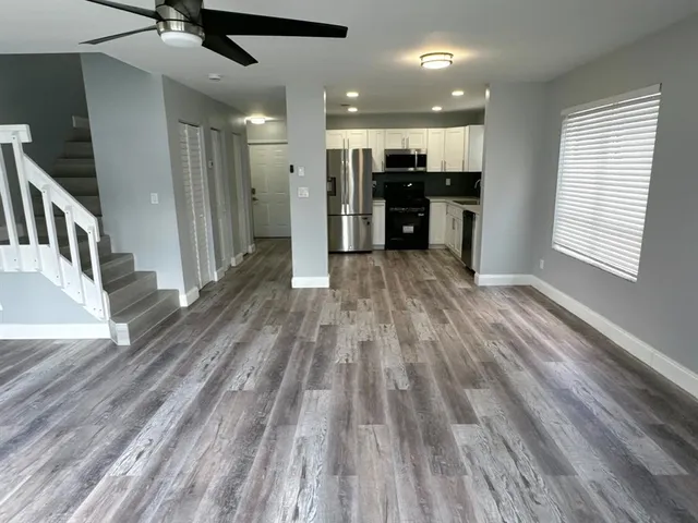 an empty room with wooden floor chandelier fan and windows