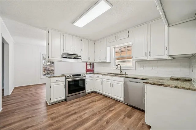 a kitchen with stainless steel appliances granite countertop a stove top oven a sink and white cabinets