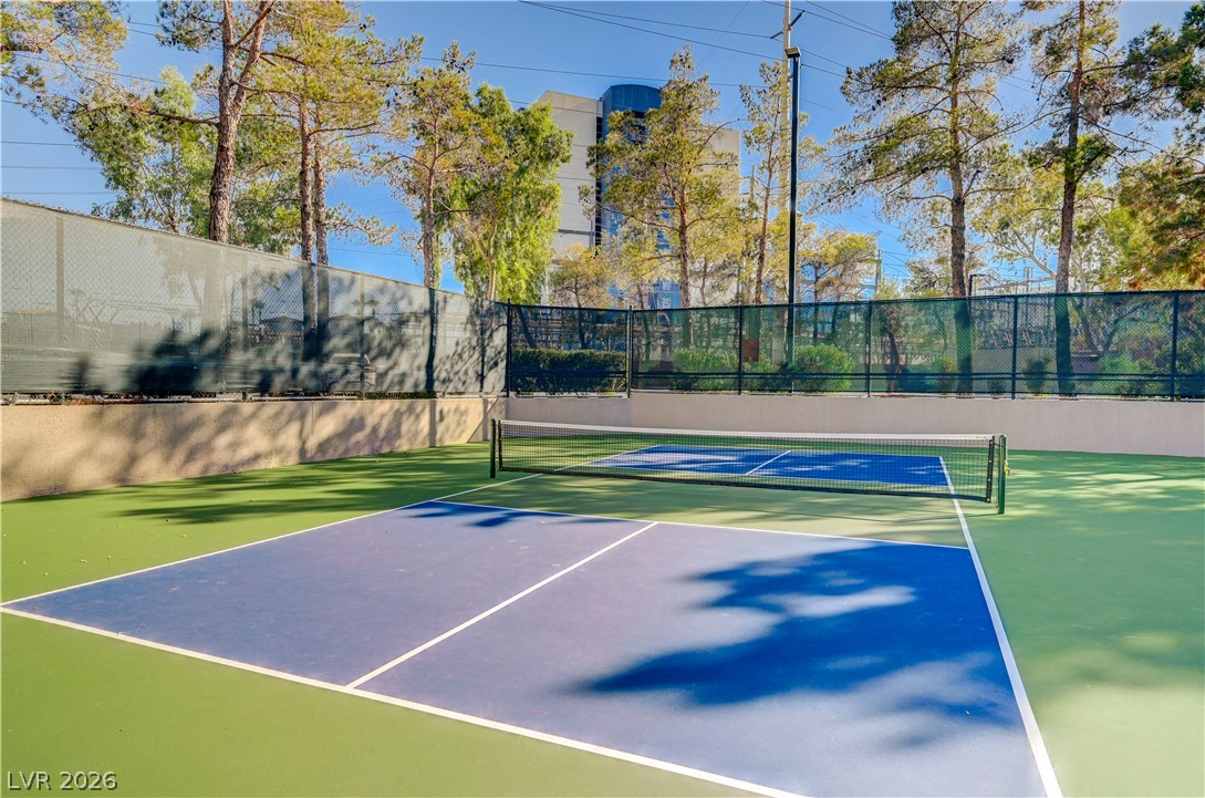 210 East Flamingo Road, Unit 112 Las Vegas, NV 89169 - Photo 57 of 59 Mature trees frame the fenced tennis court under bright blue skies.