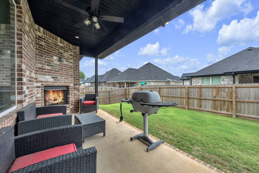 418 Casella Street Springdale, AR 72762 - Photo 30 of 34 Covered patio with brick fireplace, ceiling fan, concrete flooring, and direct access to a fenced backyard featuring a manicured lawn