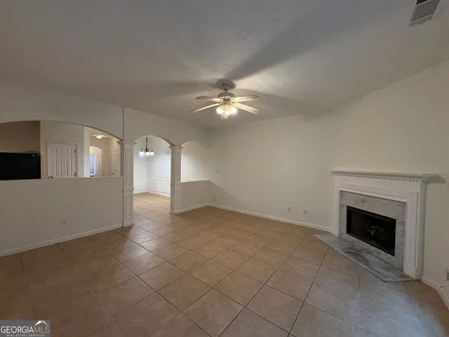 a view of an empty room with chandelier fan and fire place