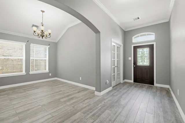 an empty room with wooden floor chandelier and windows