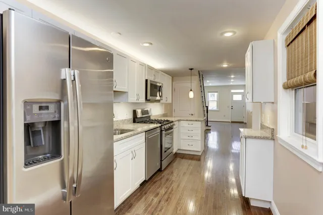 a kitchen with stainless steel appliances granite countertop a refrigerator a sink dishwasher a stove and white countertops with wooden floor