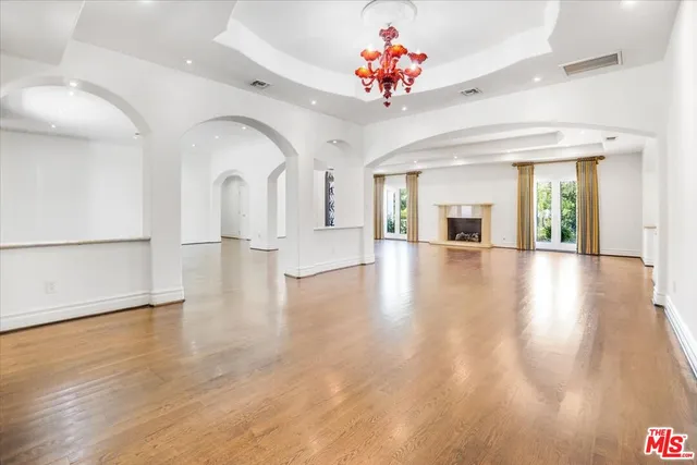 an empty room with wooden floor chandelier and windows