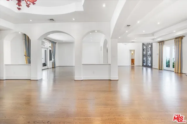 an empty room with wooden floor chandelier and windows
