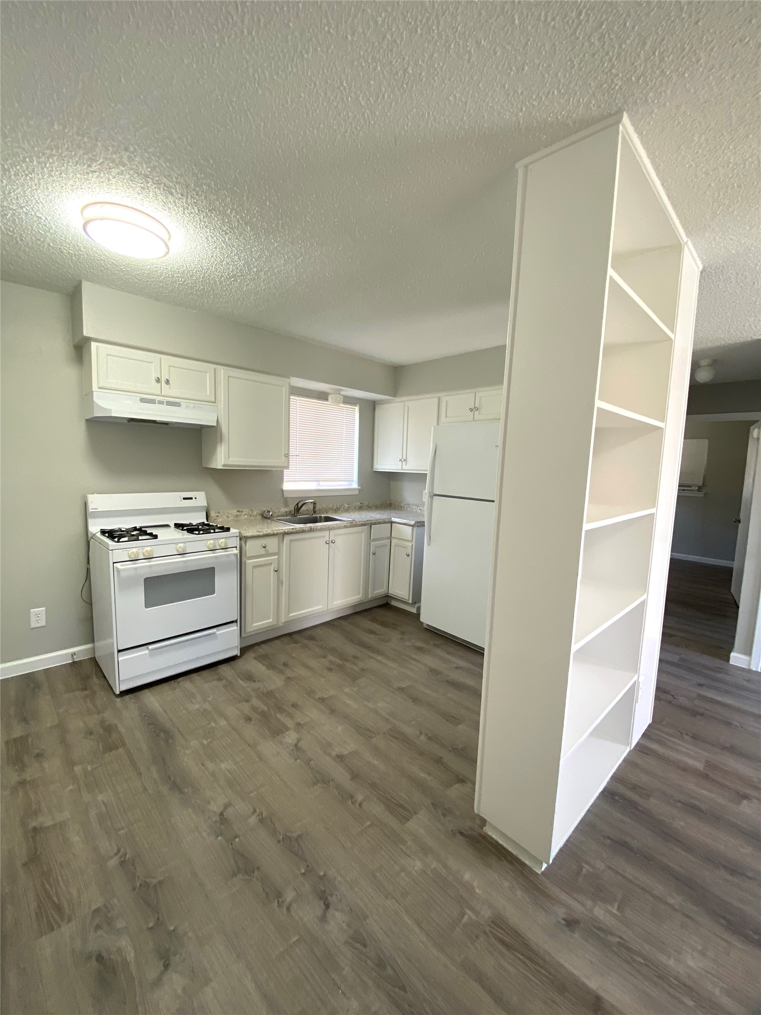 404 Swanee Drive, Unit B Austin, TX 78752 - Photo 3 of 5 Kitchen featuring a textured ceiling, white appliances, white cabinets, light countertops, and dark wood-type flooring