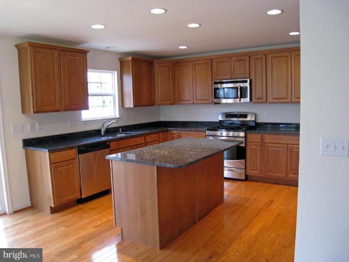 8012 Clark Station Road Severn, MD 21144 - Photo 5 of 8 a kitchen with stainless steel appliances granite countertop wooden cabinets a stove a sink and a microwave