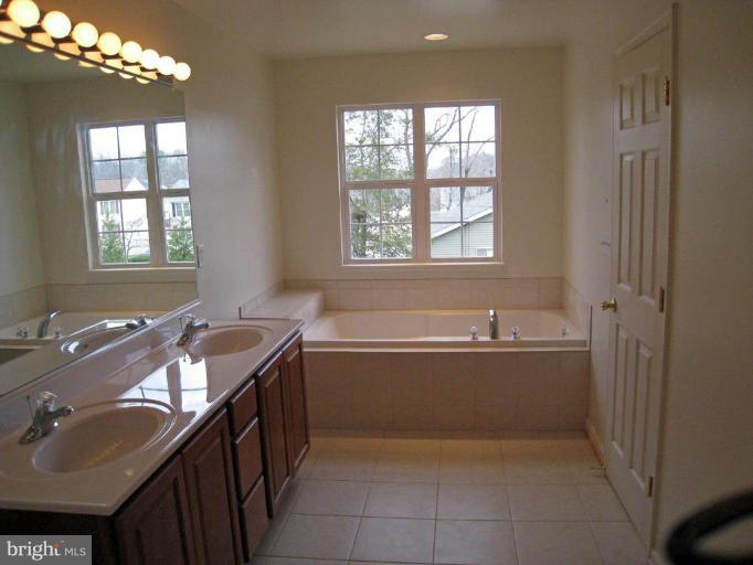 8012 Clark Station Road Severn, MD 21144 - Photo 8 of 8 a bathroom with a tub double vanity sink a mirror and a bathtub