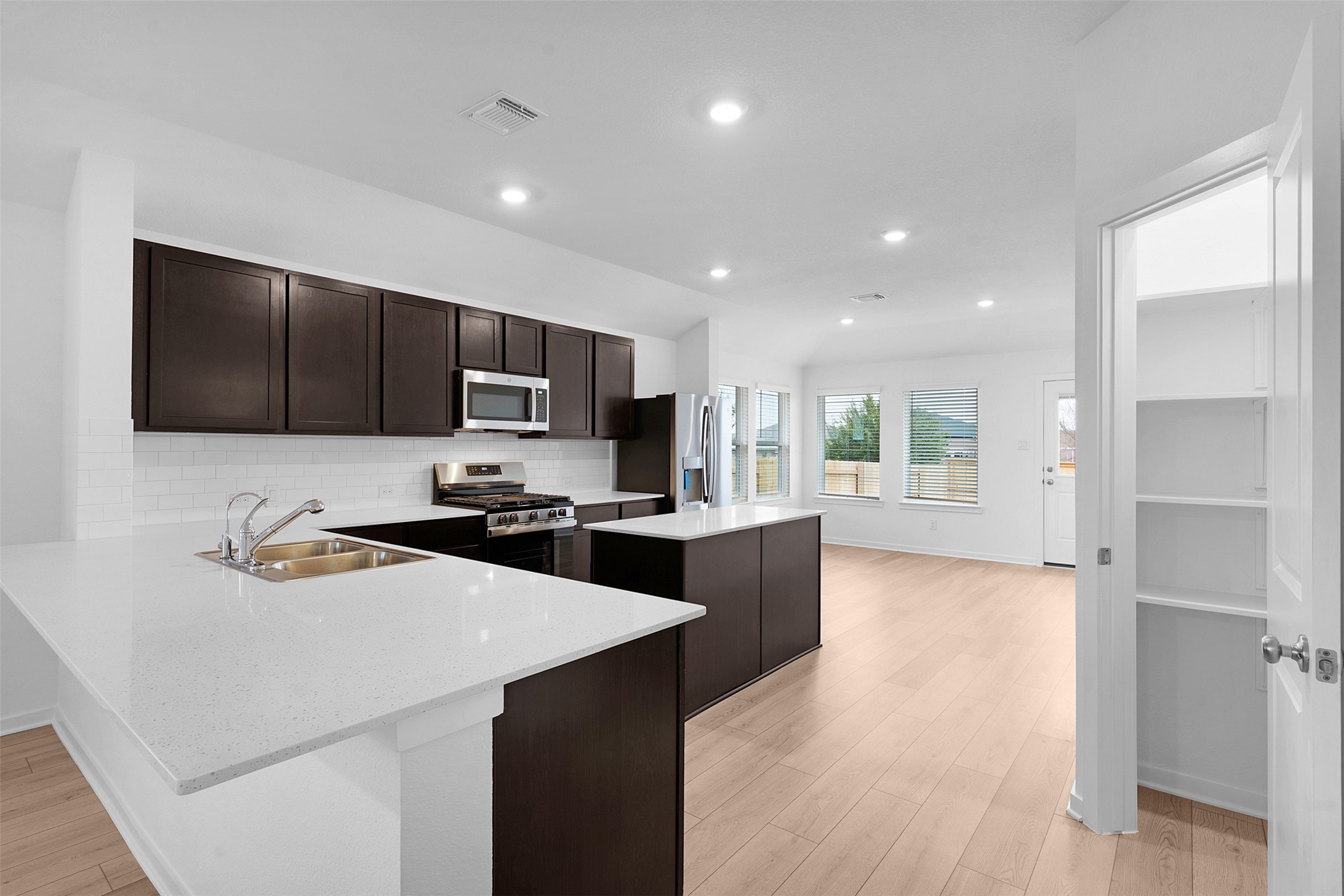 13721 Tucker Hedge Pass Elgin, TX 78621 - Photo 7 of 28 Kitchen featuring dark brown cabinetry, a kitchen island, stainless steel appliances, light stone countertops, and a peninsula