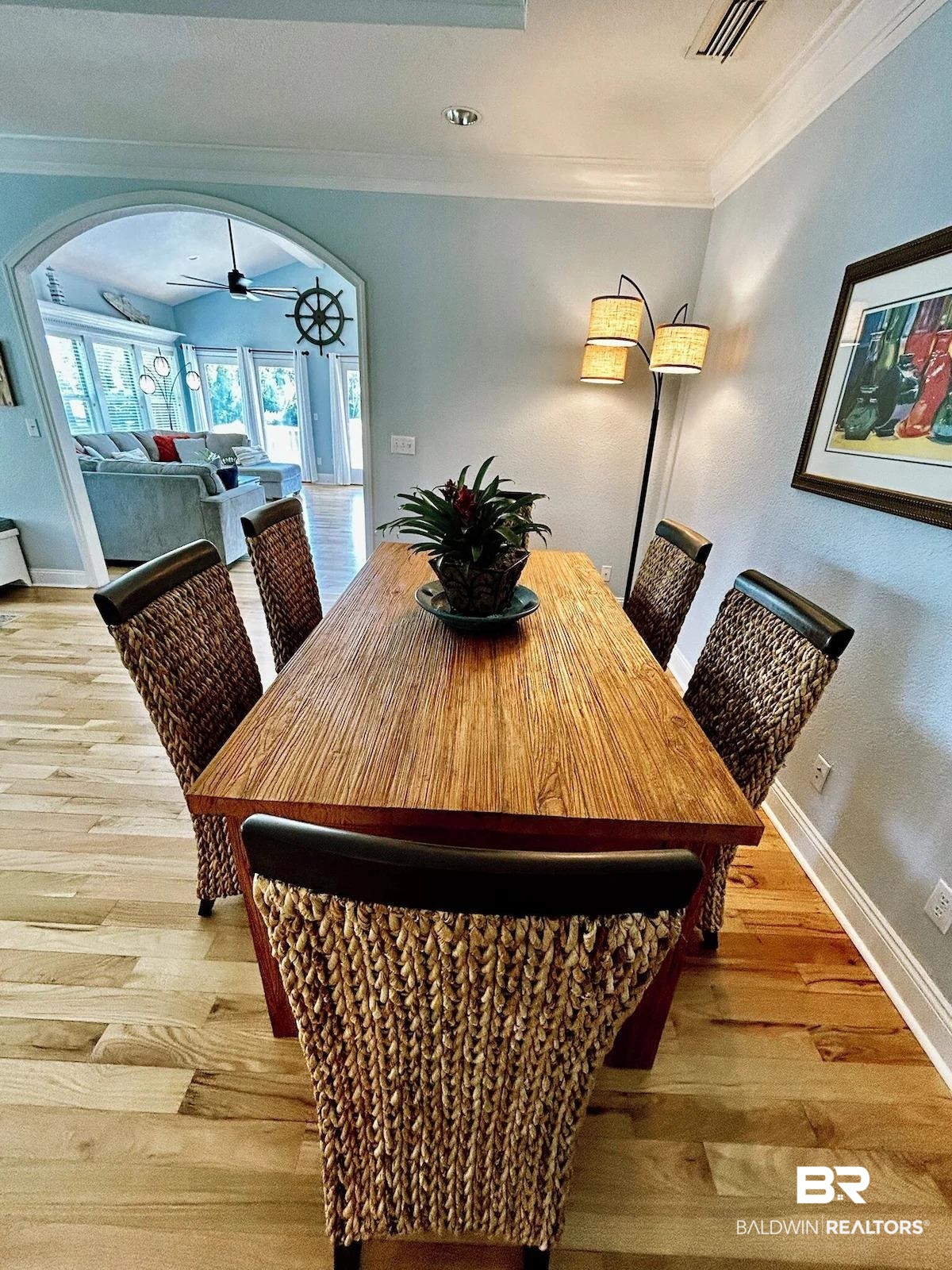 16297 Honey Road Summerdale, AL 36580 - Photo 11 of 24 Dining area featuring wood-finish flooring, a wood-finish dining table, light blue wall paint, and an arched doorway opening to an additional living space