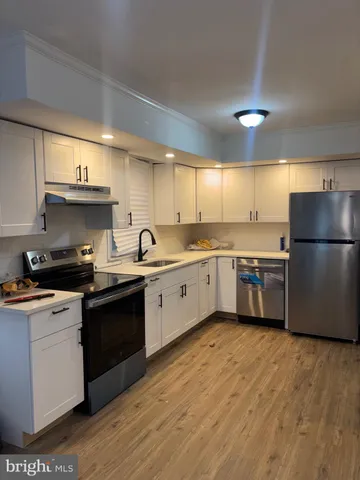 a kitchen with stainless steel appliances granite countertop a sink a stove a refrigerator with white cabinets and wooden floor