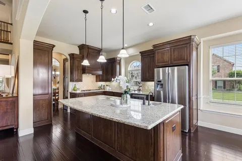a kitchen with stainless steel appliances granite countertop a sink a refrigerator and a wooden floor
