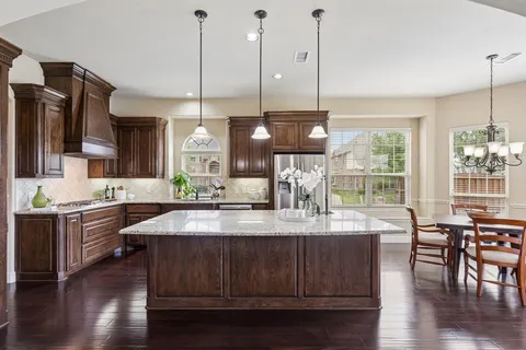 a kitchen with stainless steel appliances granite countertop wooden floors wooden cabinets a dining table and chairs