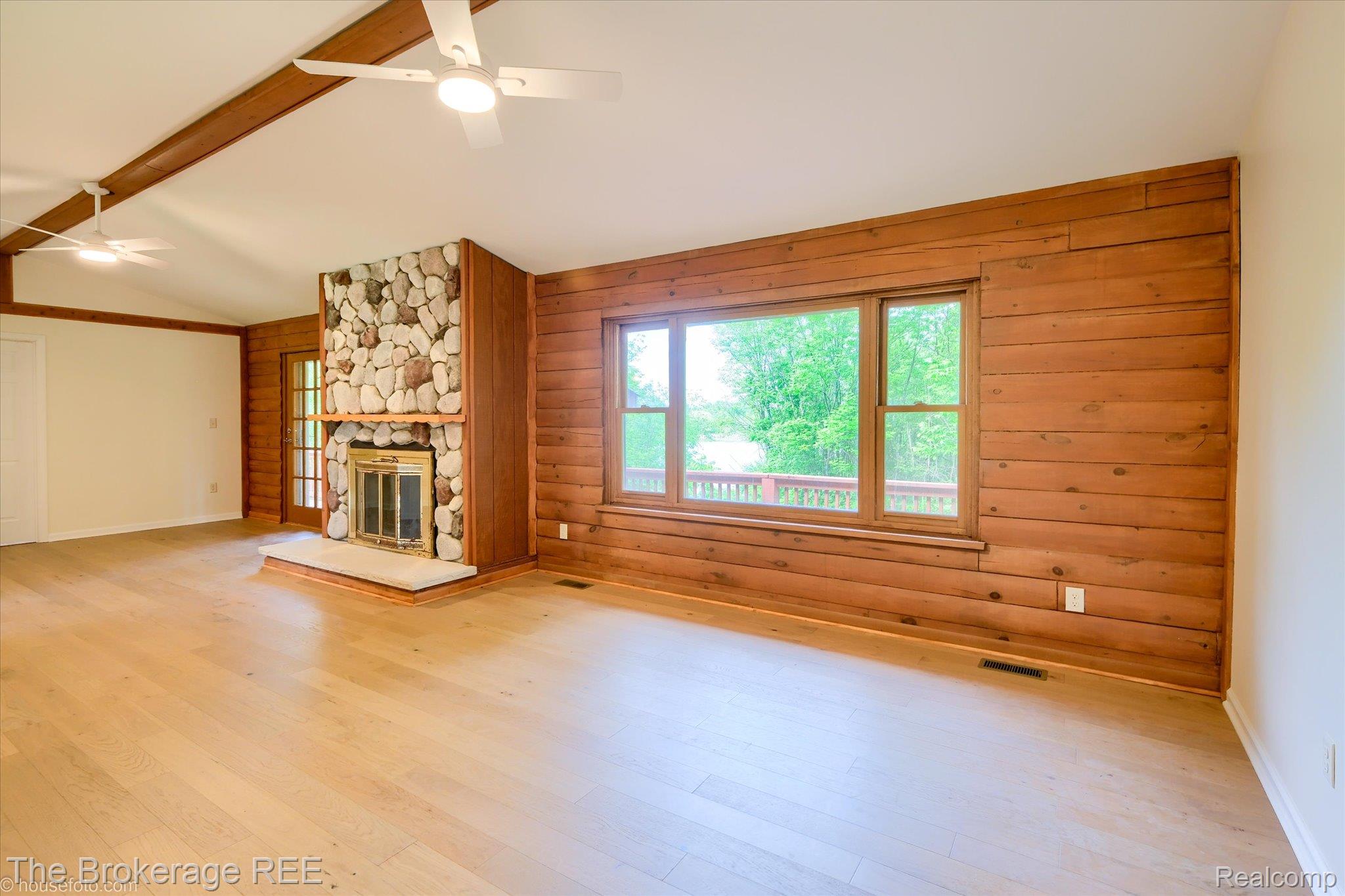 1077 Hadley Road Lapeer, MI 48446 - Photo 8 of 61 Spacious interior featuring a stone fireplace with hearth, wood-finish flooring, exposed ceiling beams, and a wood-paneled accent wall with large windows